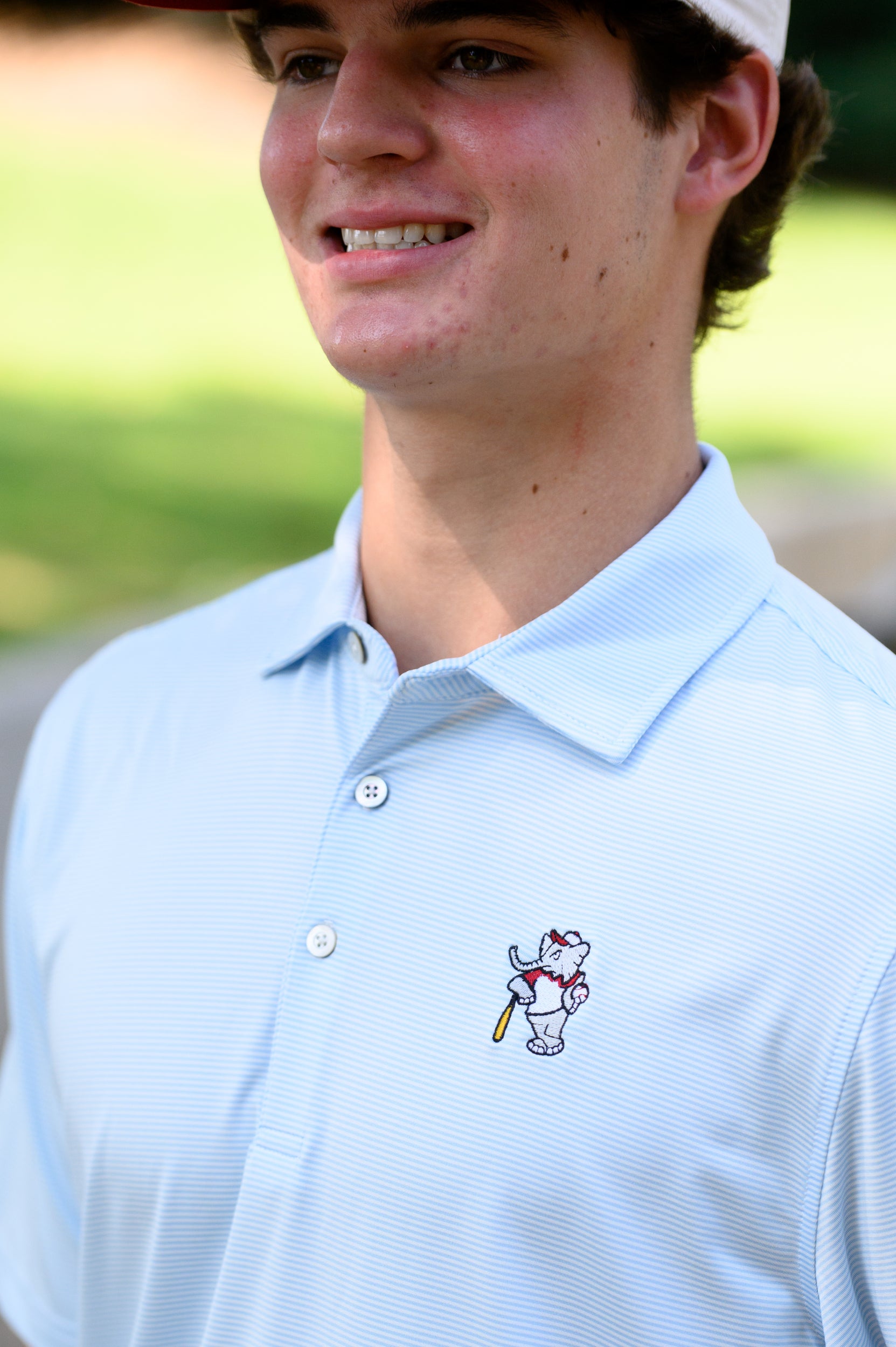 University of Alabama BallPlayer Al Men's Light Blue Performance Polo with an embroidered image of Big Al in a baseball uniform leaning on a baseball bat