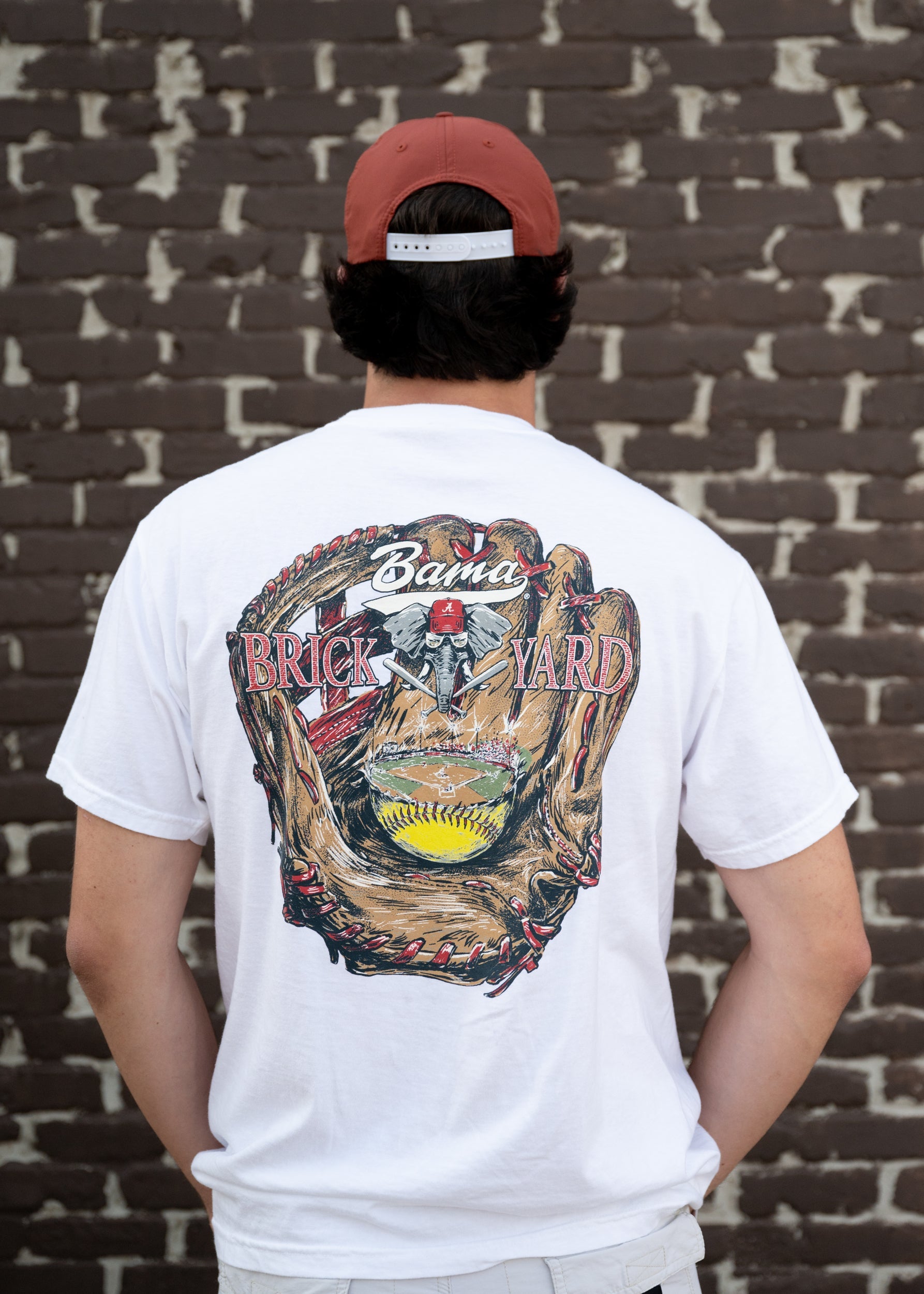 University of Alabama Bama Brick Yard White Comfort Colors T-Shirt with an image of a baseball glove catching a baseball field beneath the text "Bama Brick Yard"