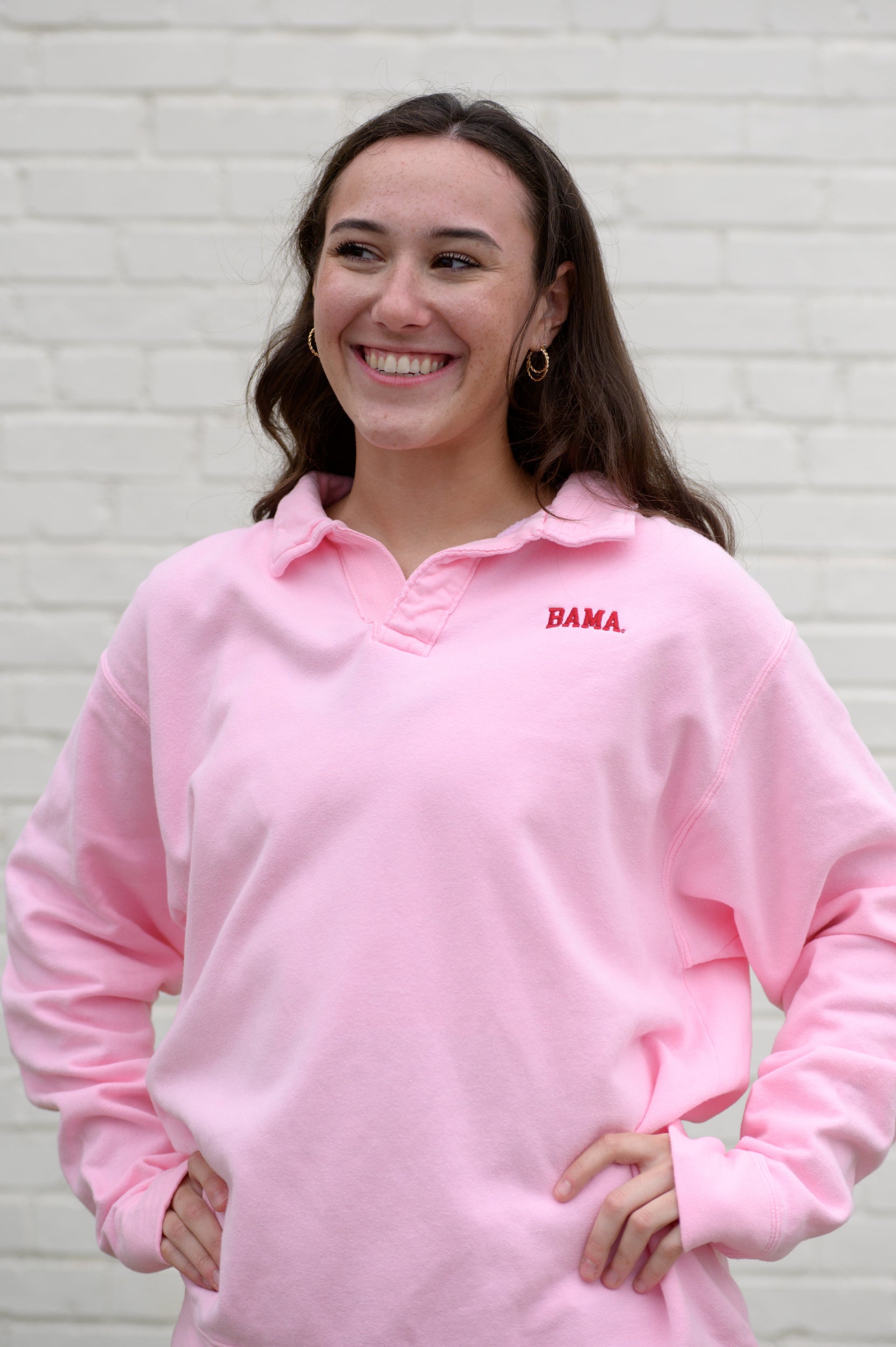 Woman wearing a pink collared sweatshirt with 'BAMA' embroidered in crimson on it.