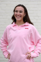 Woman wearing a pink collared sweatshirt with 'BAMA' embroidered in crimson on it.