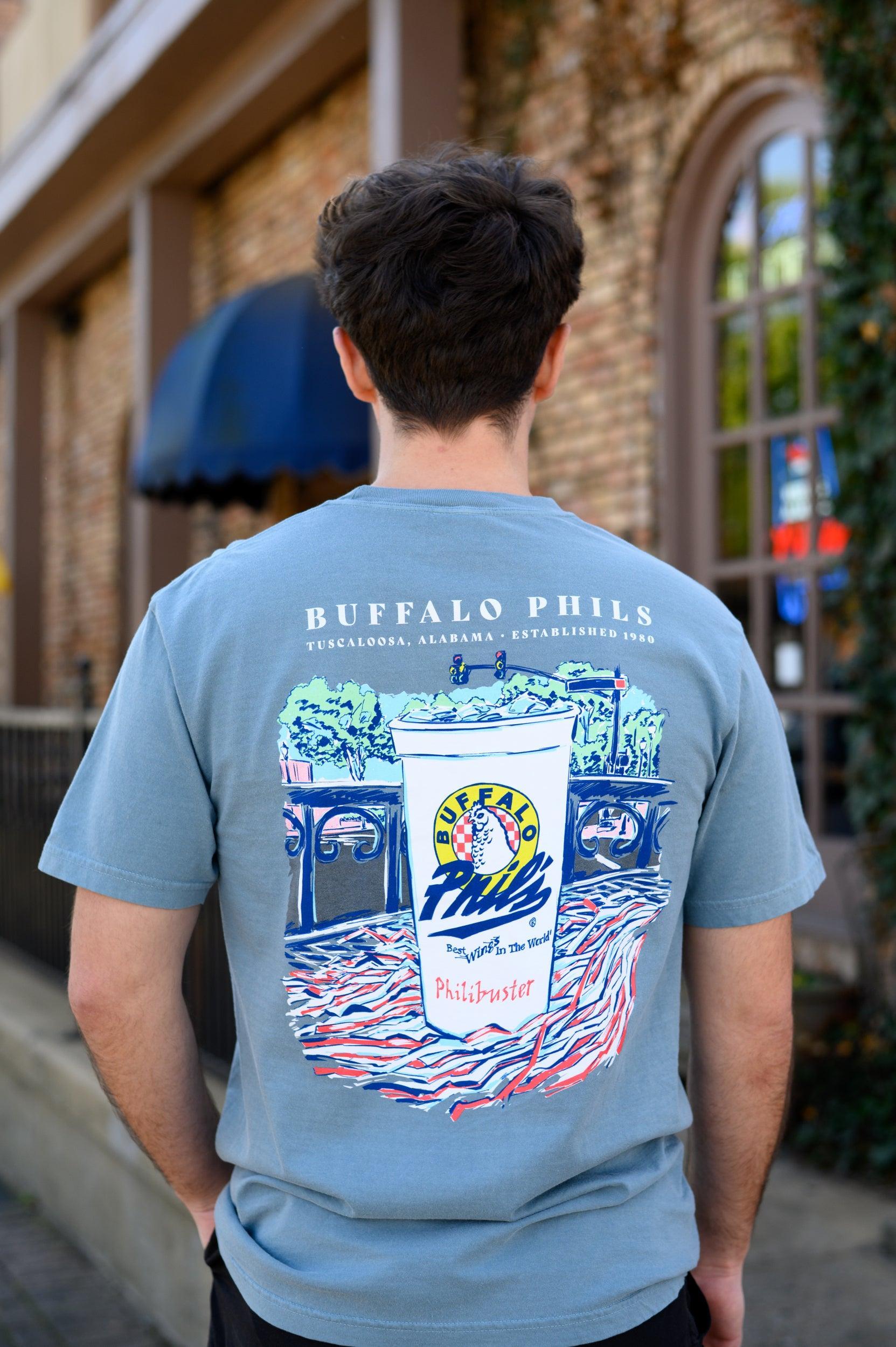 Ice Blue Buffalo Phil's T-Shirt with an image of a Buffalo Phil's cup sitting on top of a shaker on a table looking out on The Strip