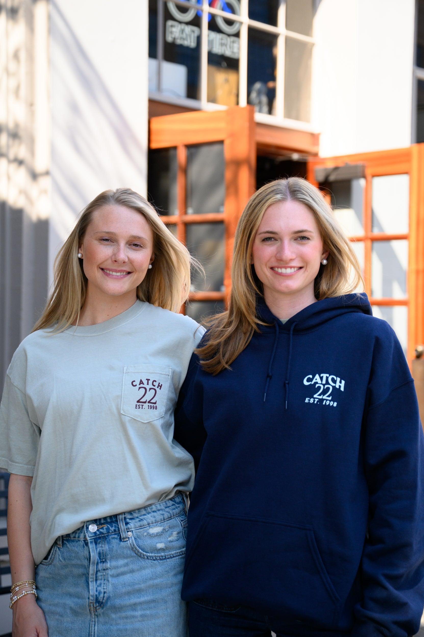 Two women wearing 'Catch 22' branded clothing standing outside a building.