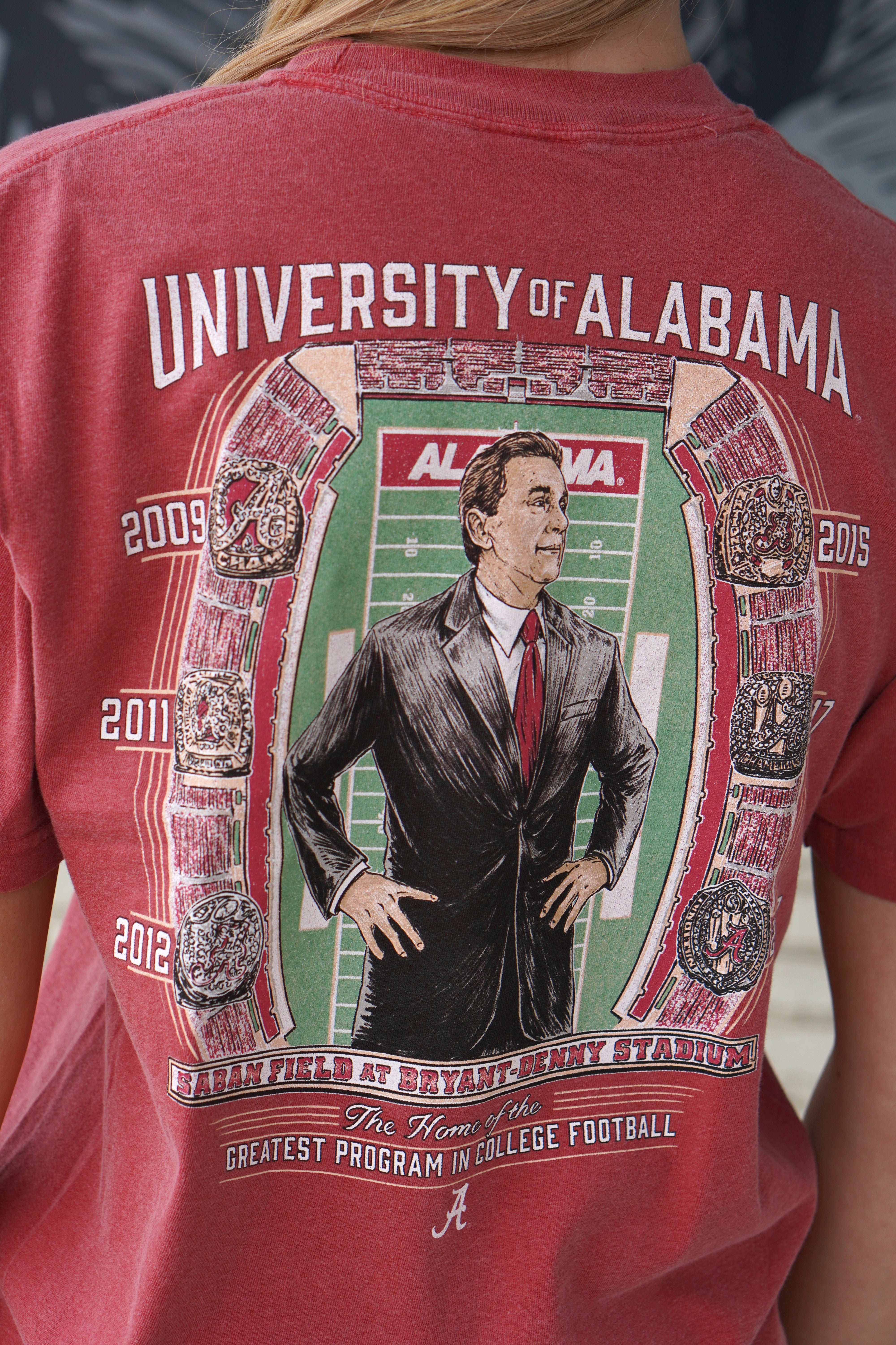 University of Alabama Champion Legacy at Saban Field Red Comfort Colors T-Shirt with an image of Nick Saban standing over Bryant-Denny Stadium surrounded by the years Alabama won the Football Championship