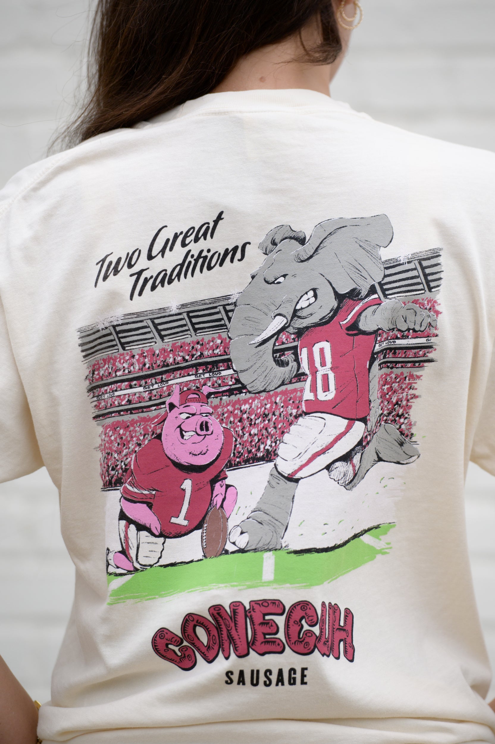 University of Alabama Conecuh Traditions Ivory Comfort Colors T-Shirt with Black text "Two Great Traditions" above an illustration of a pig holding a football for Big Al to kick 