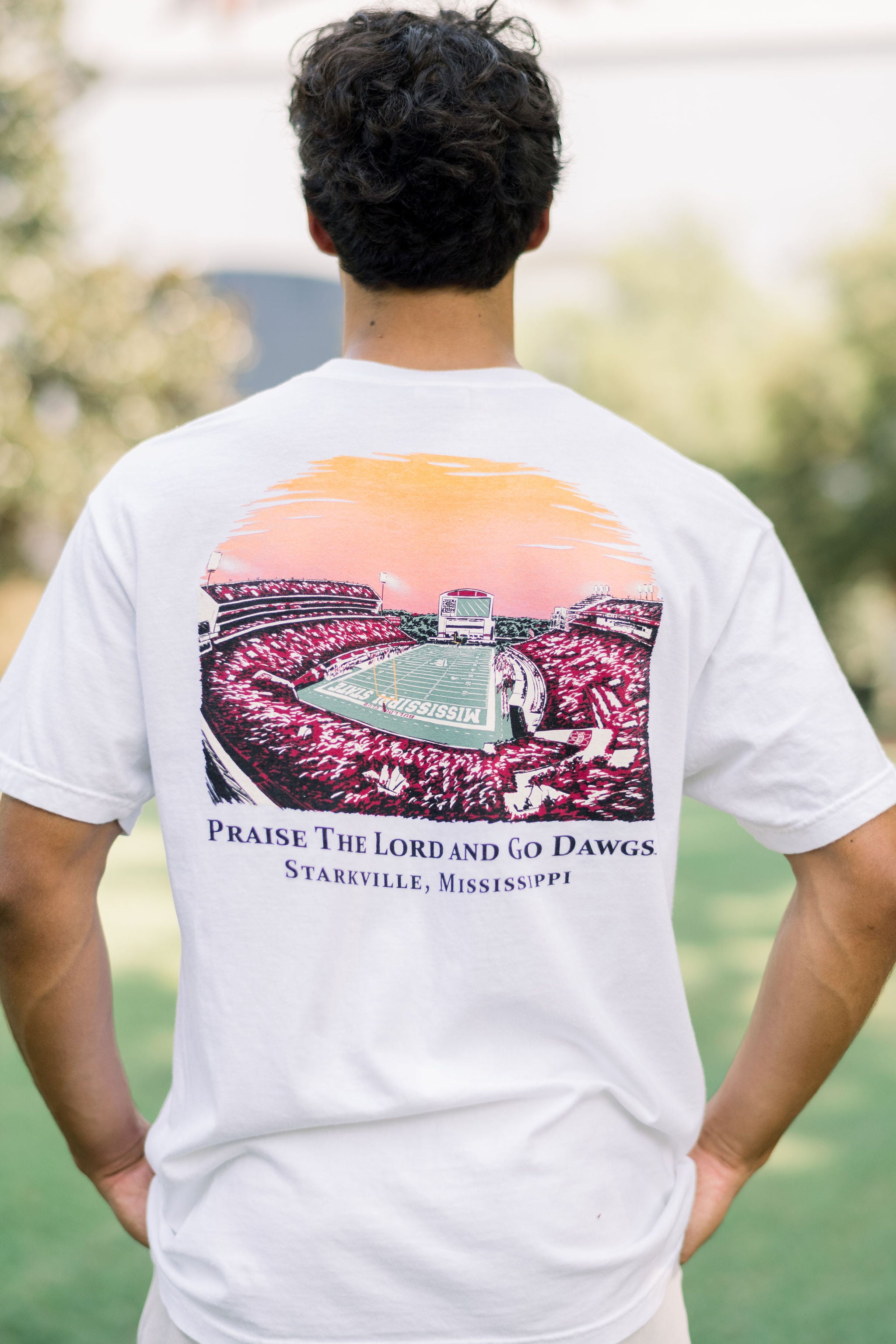 Mississippi State White T-Shirt with an image of the sun setting over the crowded Davis-Wade Stadium above text “Praise The Lord And Go Dawgs”
