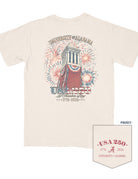 University of Alabama Ivory T-Shirt with an image of Denny Chimes decorated in Americana banners and fireworks exploding behind it with text “USA 250”