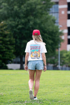 University of Alabama White Denny Dogs Comfort Colors T-Shirt with an image of two hands holding hot dogs at Bryant- Denny Stadium above the Black text "denny dogs"