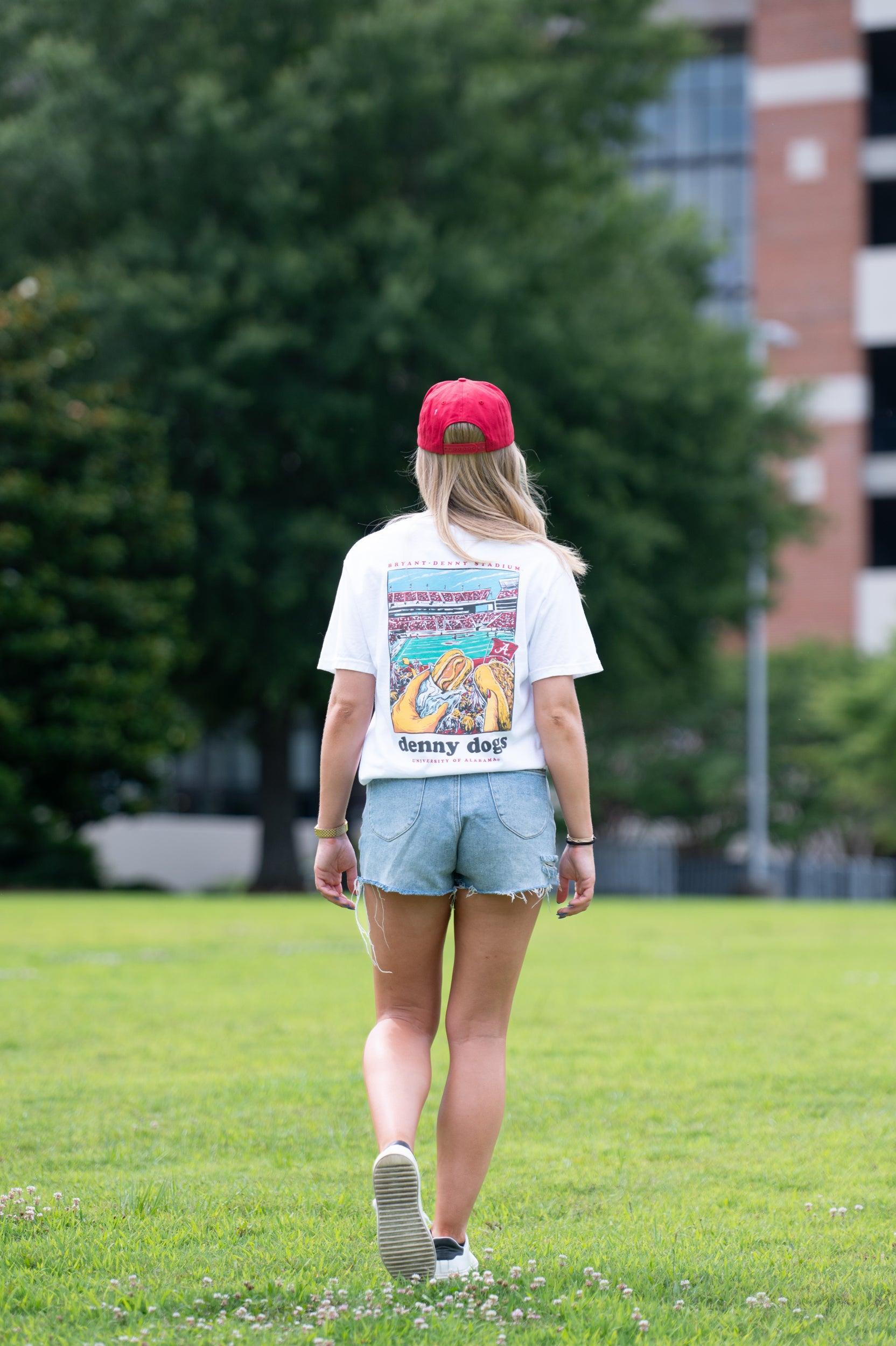 University of Alabama White Denny Dogs Comfort Colors T-Shirt with an image of two hands holding hot dogs at Bryant- Denny Stadium above the Black text "denny dogs"