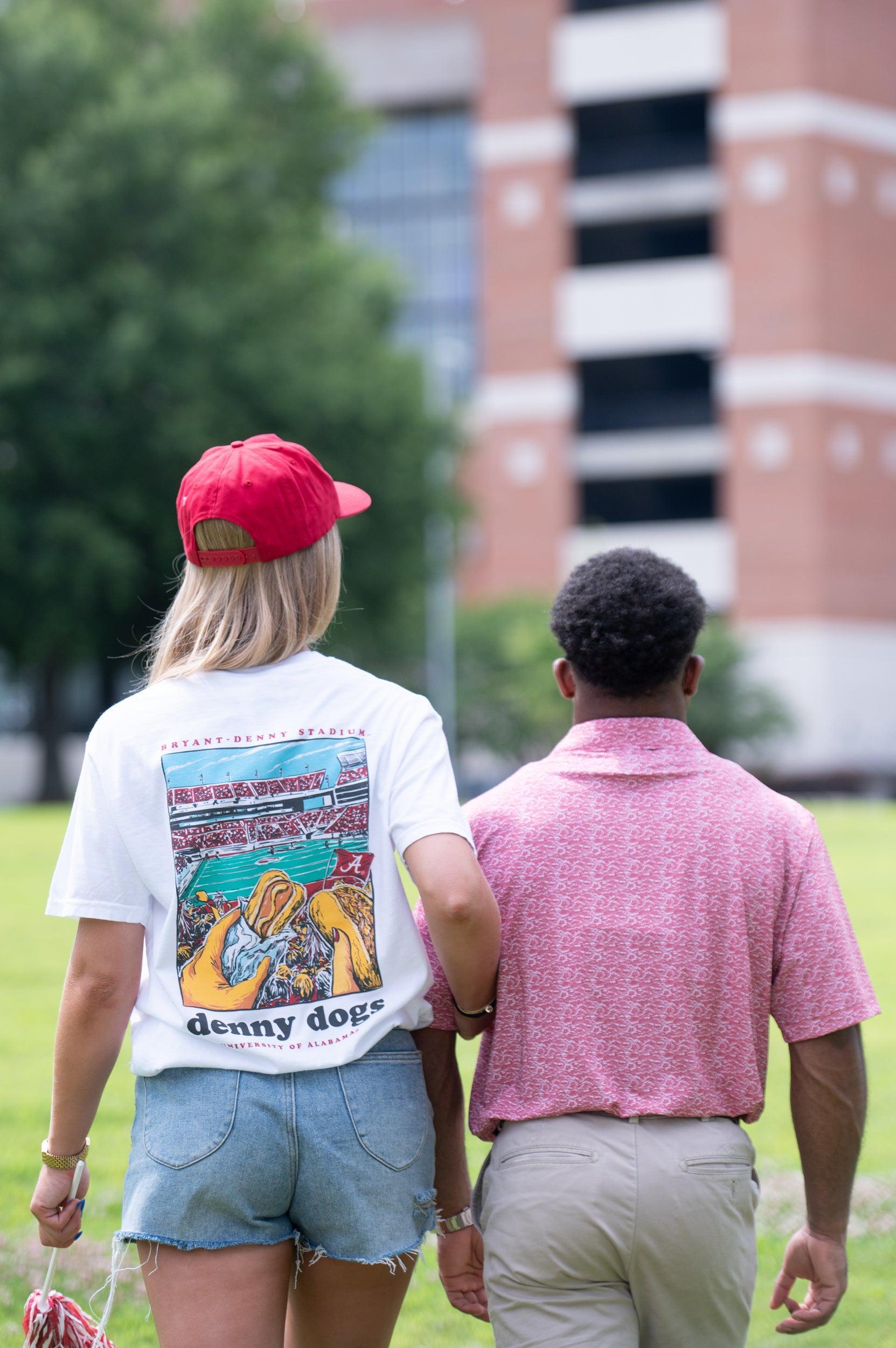 University of Alabama White Denny Dogs Comfort Colors T-Shirt with an image of two hands holding hot dogs at Bryant- Denny Stadium above the Black text "denny dogs"