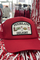 University of Alabama Red Trucker Hat with a patch featuring text “Dixieland” above and “Delight” below drawings of a cowboy boot, money, drink can, football, and playing card