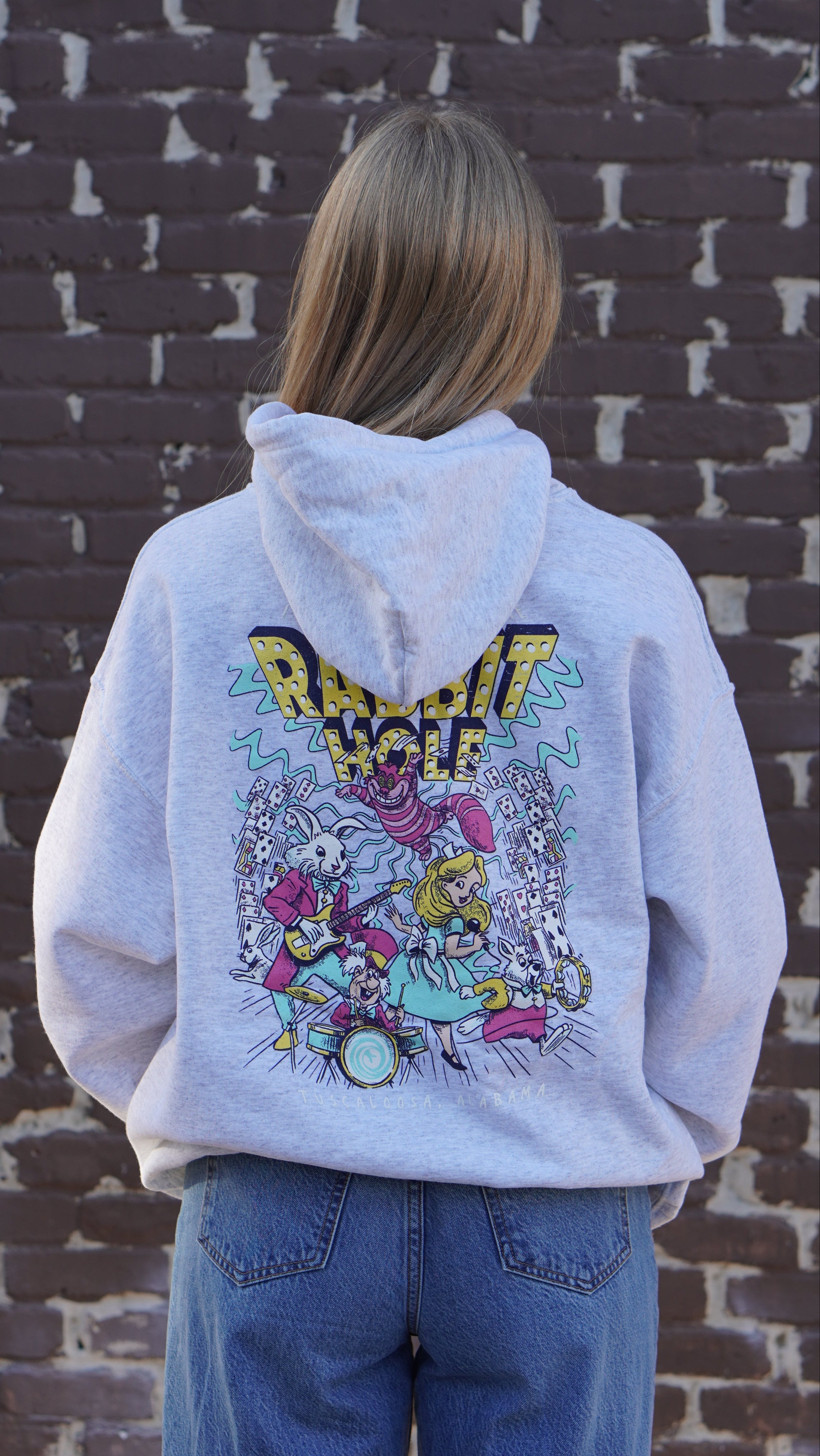 Grey Rabbit Hole Hoodie with marquee lights spelling "Rabbit Hole" lighting a band of Alice in Wonderland characters surrounded by paying cards