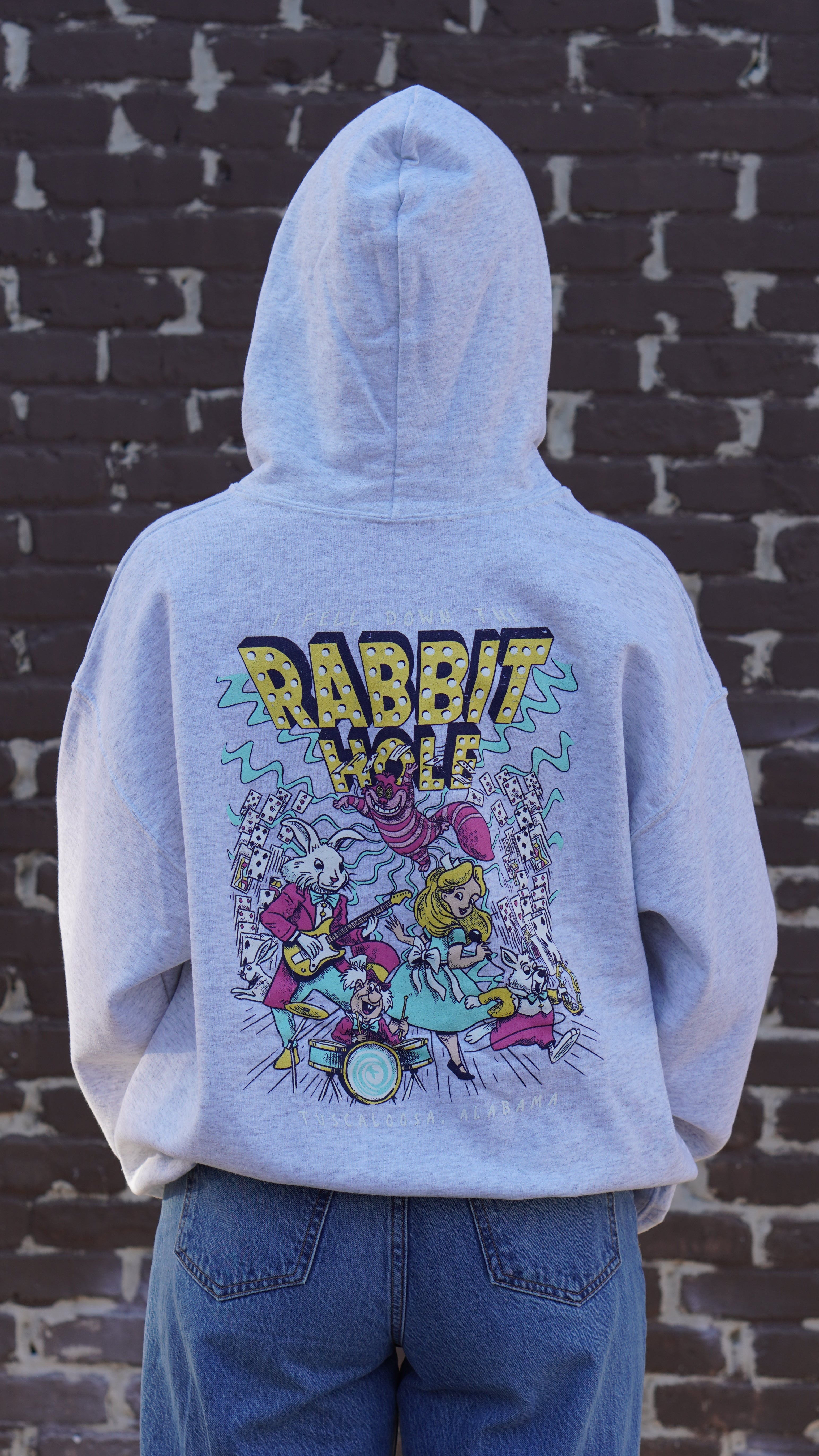 Grey Rabbit Hole Hoodie with marquee lights spelling "Rabbit Hole" lighting a band of Alice in Wonderland characters surrounded by paying cards