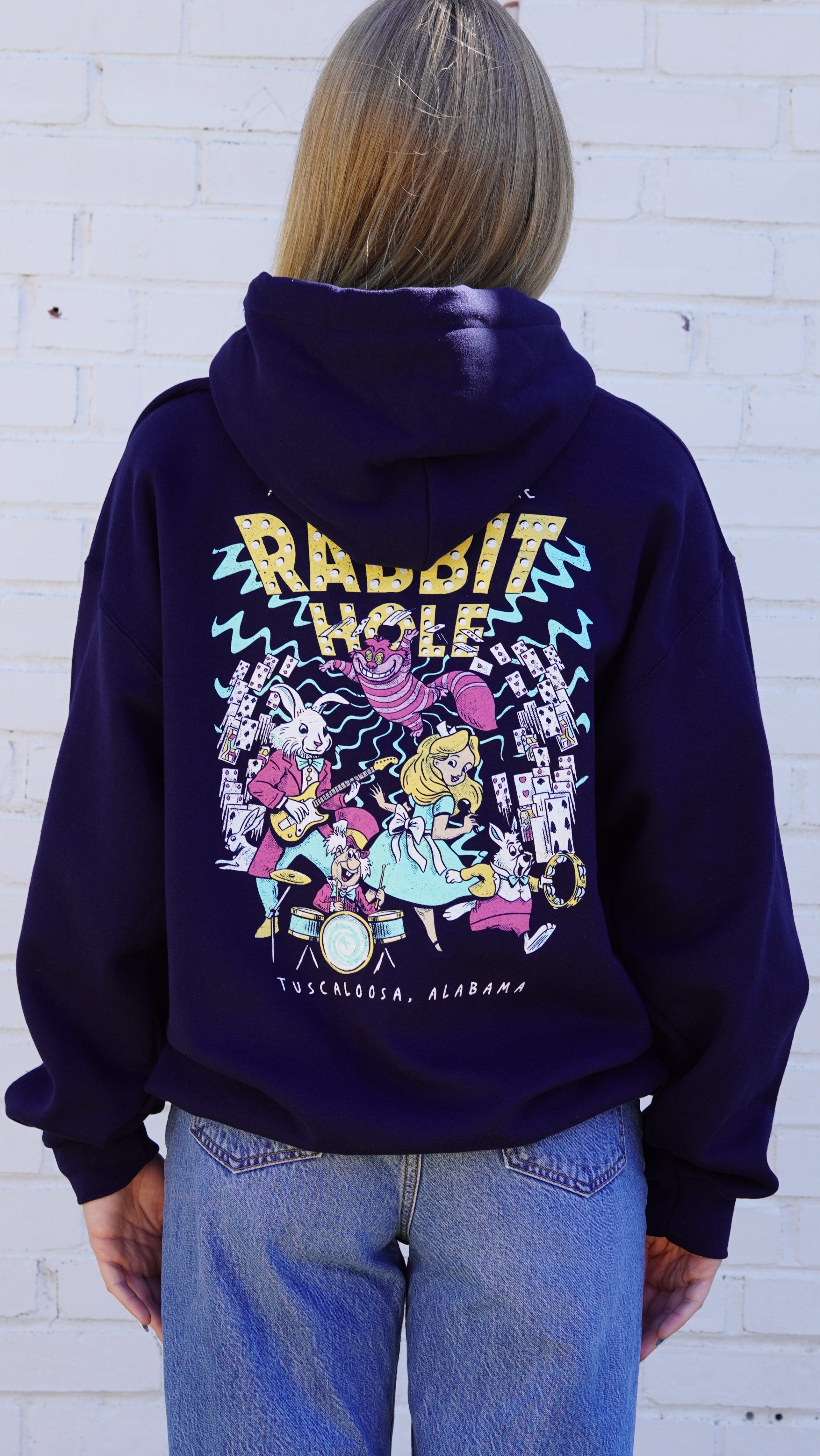Navy Rabbit Hole Hoodie with marquee lights spelling "Rabbit Hole" lighting a band of Alice in Wonderland characters surrounded by playing cards