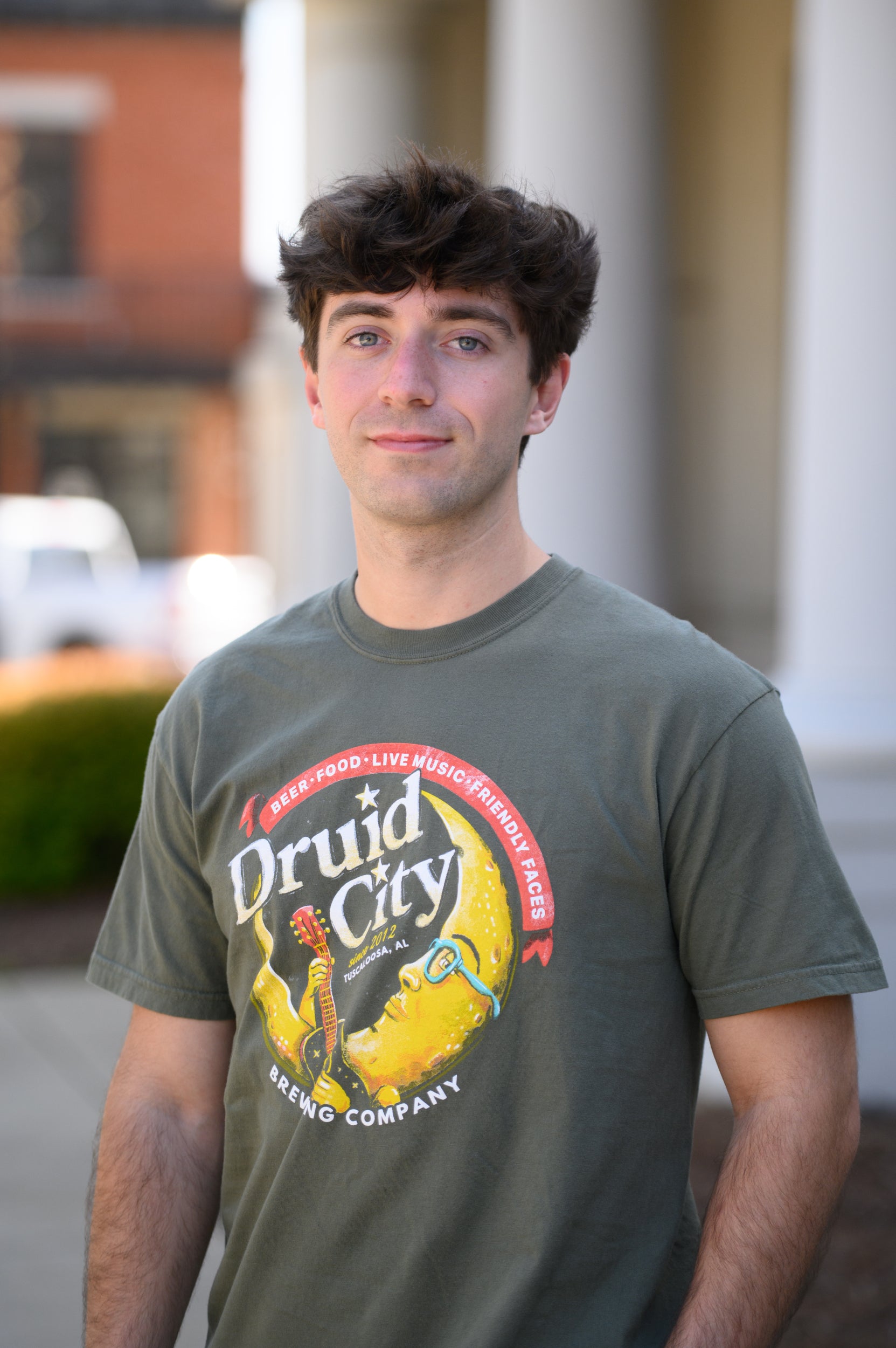 Druid City Brewing Company Olive Green Tee with text "Druid City" above a Crescent Moon wearing glasses and playing a guitar