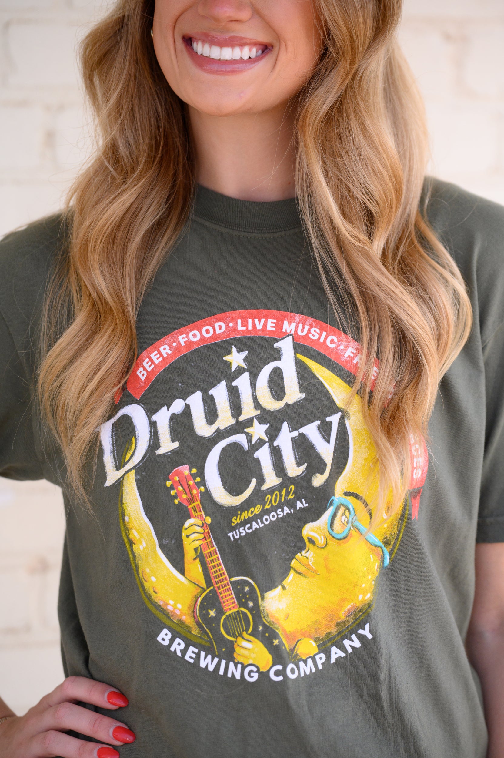 Druid City Brewing Company Olive Green Tee with text "Druid City" above a Crescent Moon wearing glasses and playing a guitar