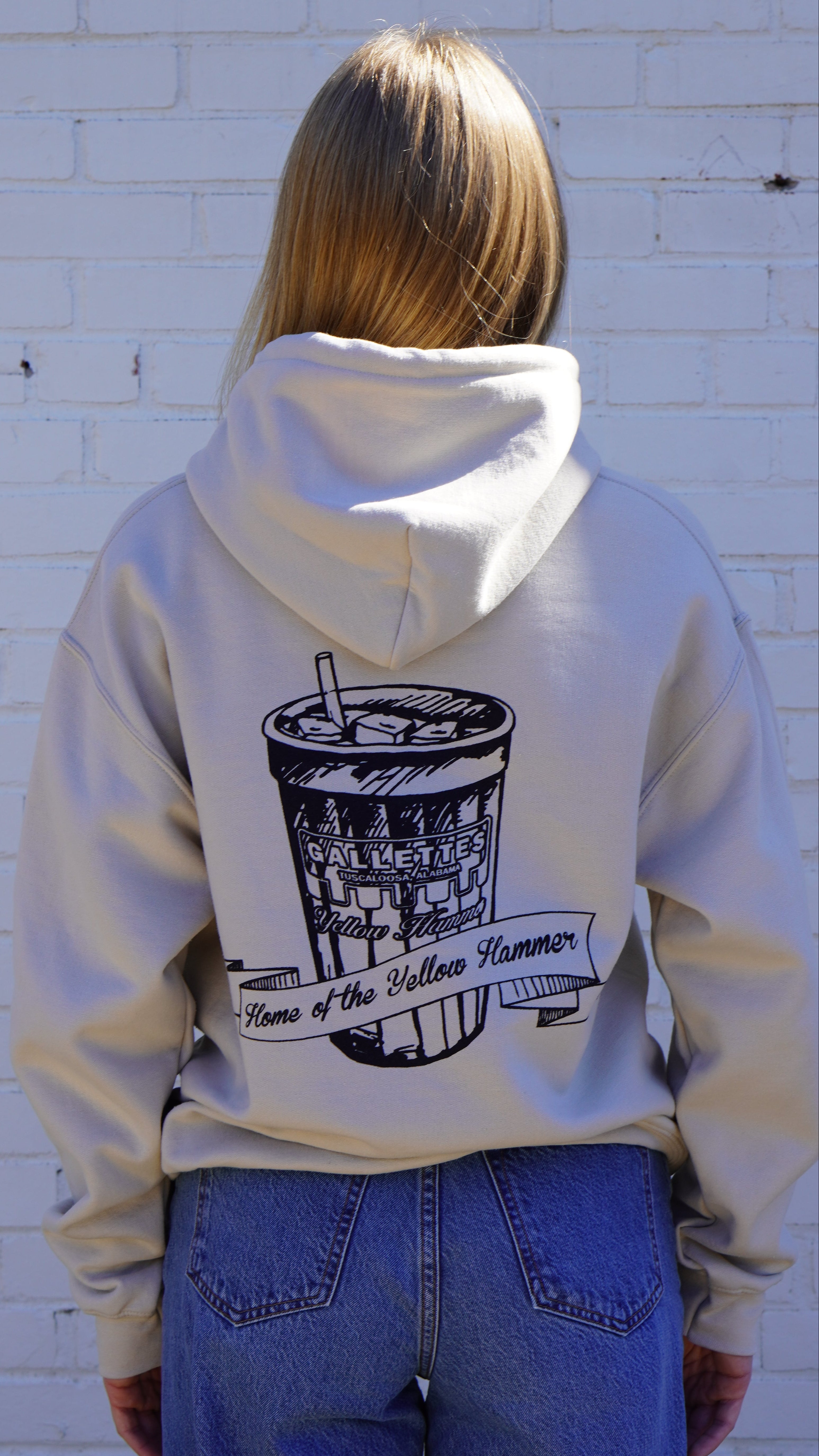 Gallettes Tan Hoodie with an illustration of a yellow hammer drink with a sash that reads “home of the yellow hammer”