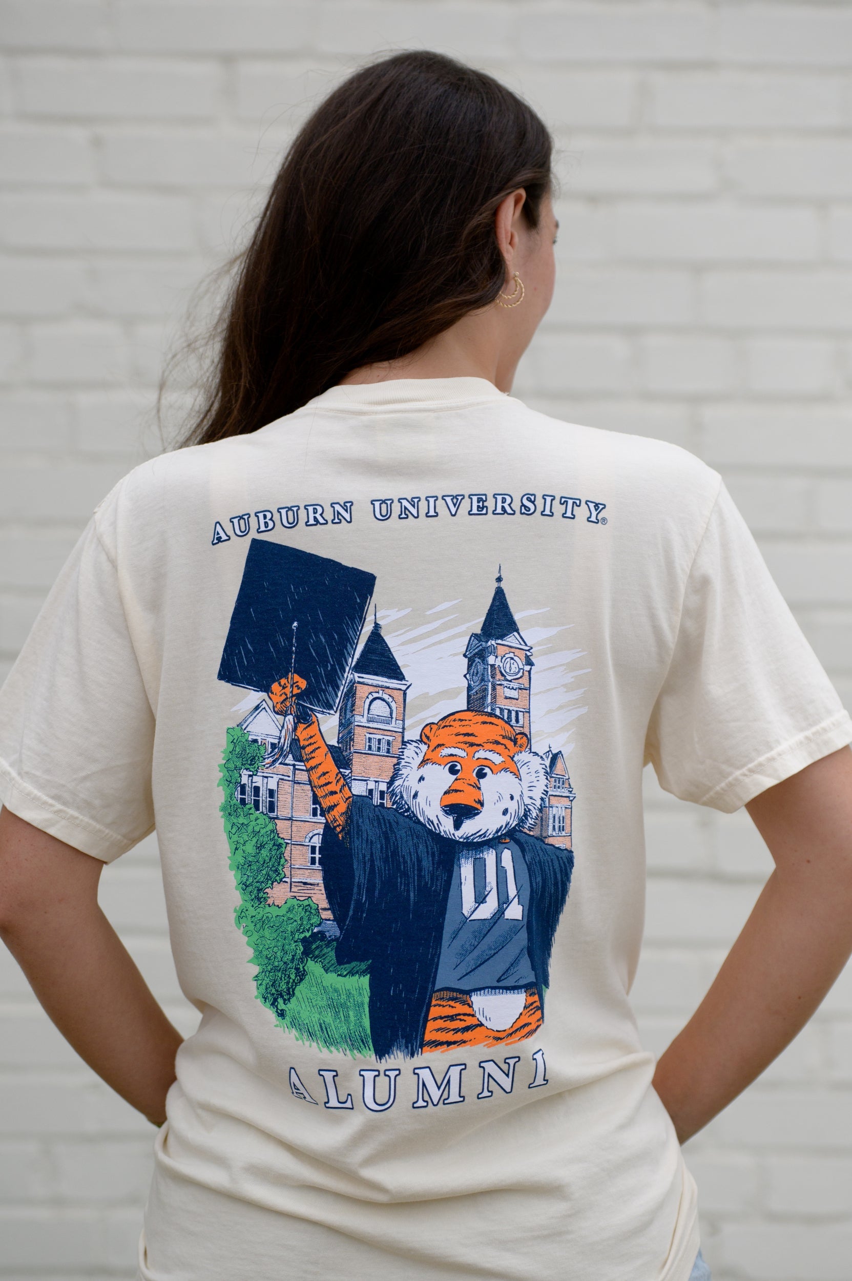 Auburn University Cream Aubie Graduation T-Shirt with an image of Aubie in graduation attire in front of Samford Hall above White text "Alumni”