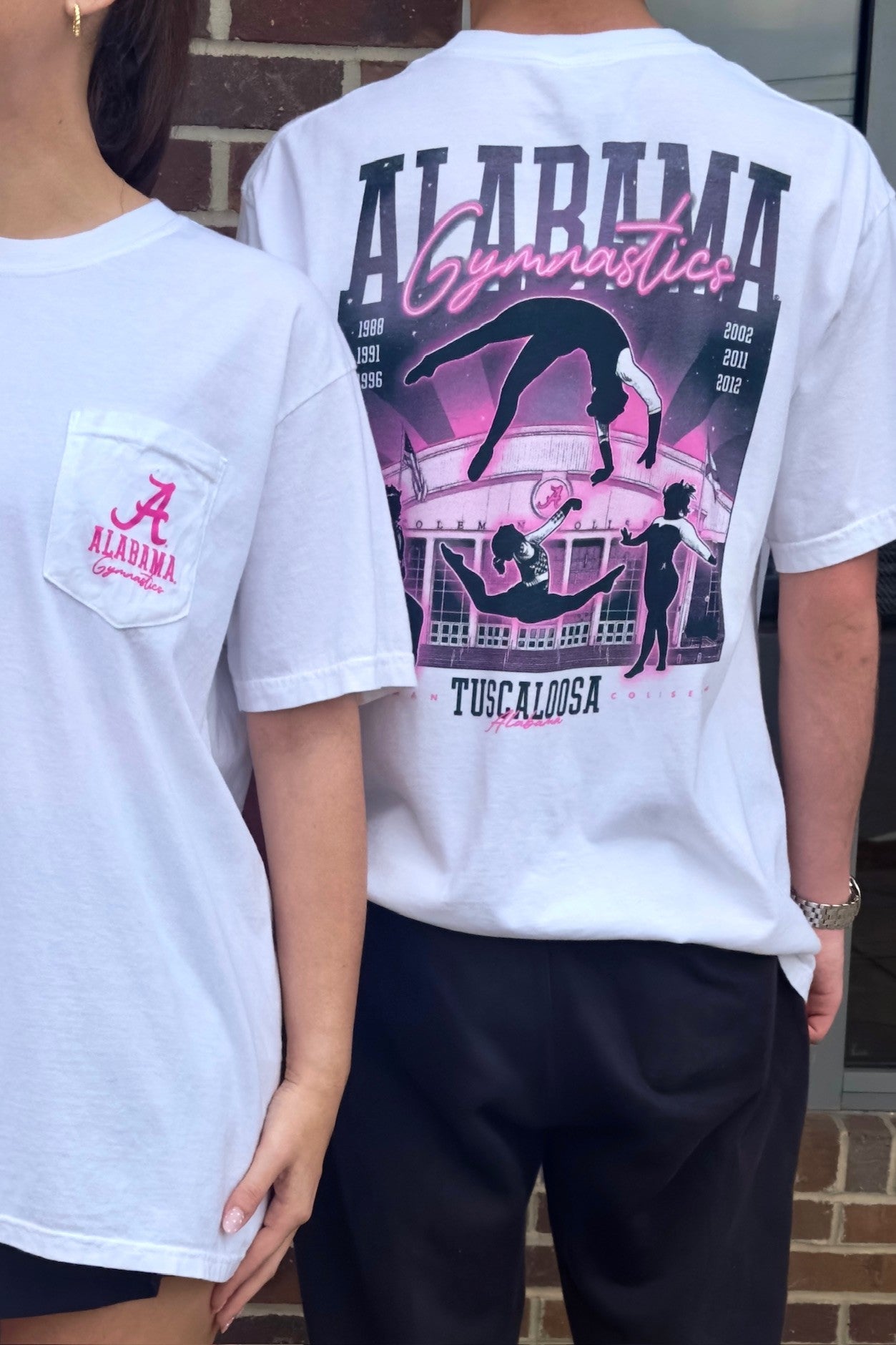 University of Alabama White Ladies' Gymnastics T-Shirt with a hand-drawn design featuring Coleman Coliseum and the years of the Crimson Tide's national titles.