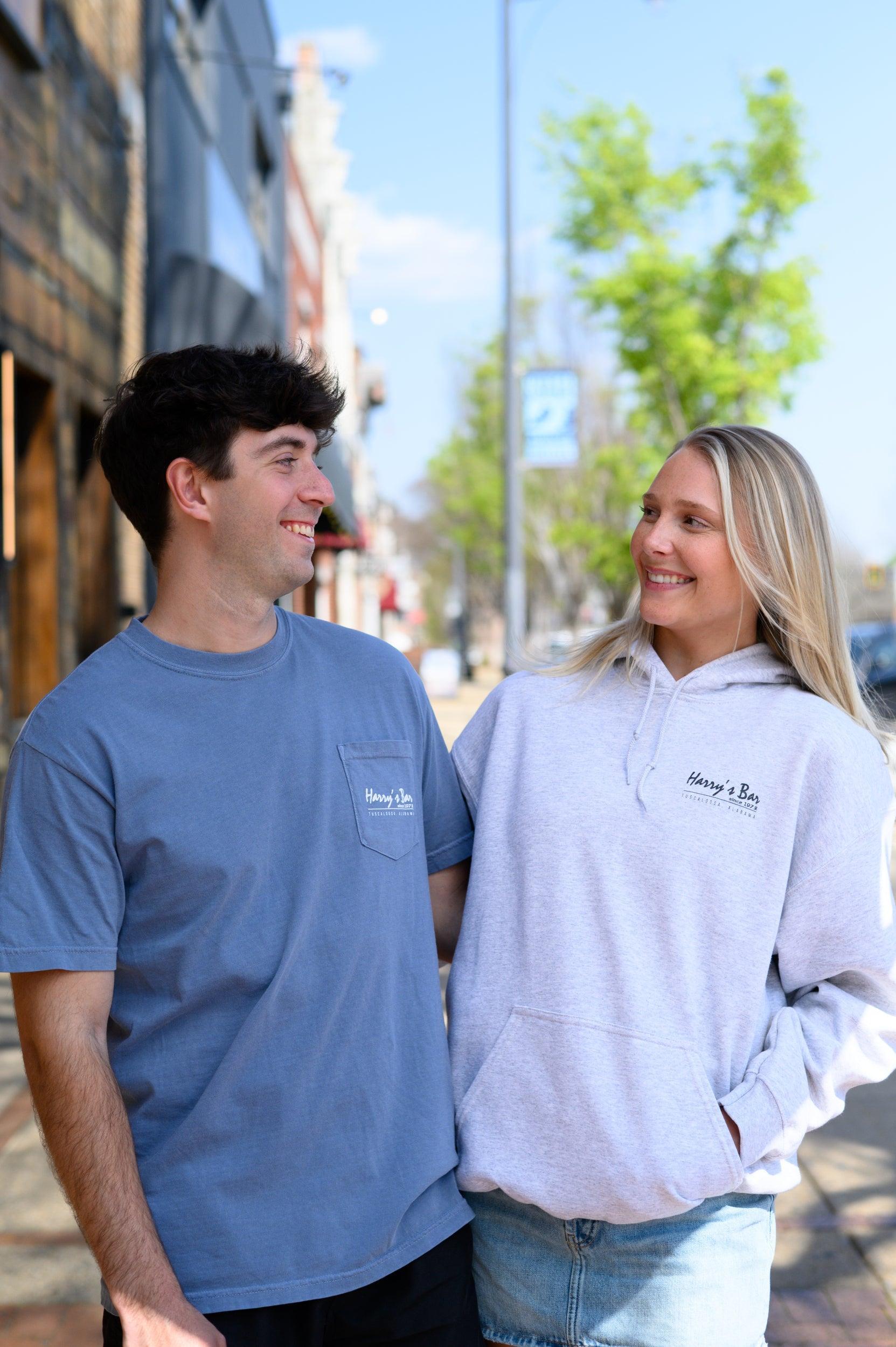 Two people wearing Harry's Bar branded clothing standing on a street.