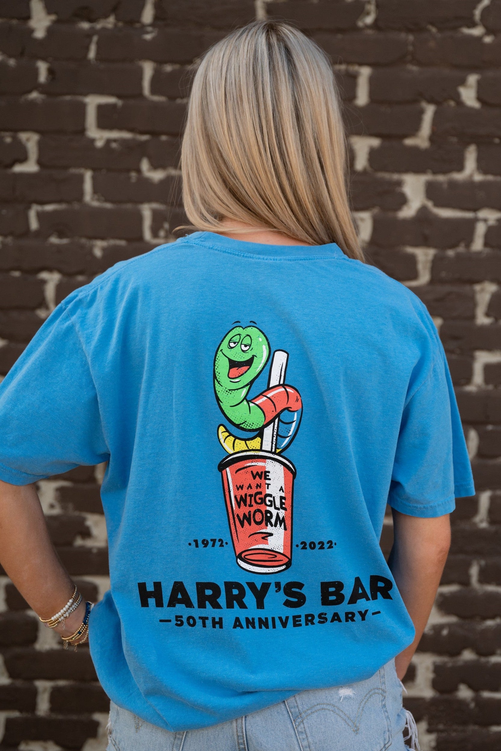 Harry's Bar Blue Shirt with a cartoon of the Wiggle Worm Drink above Black text “Harry’s Bar”