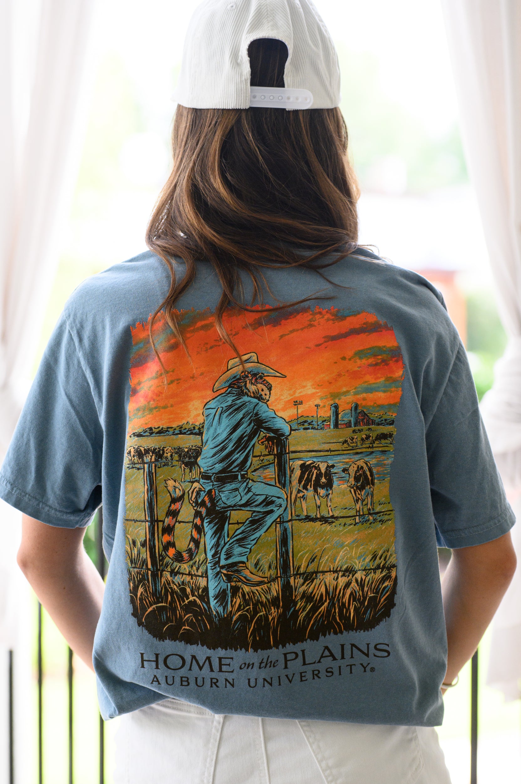 Auburn University Blue T-Shirt with an image of Aubie wearing cowboy clothes and watching over cattle at sunrise above Black text “Home on the Plains”