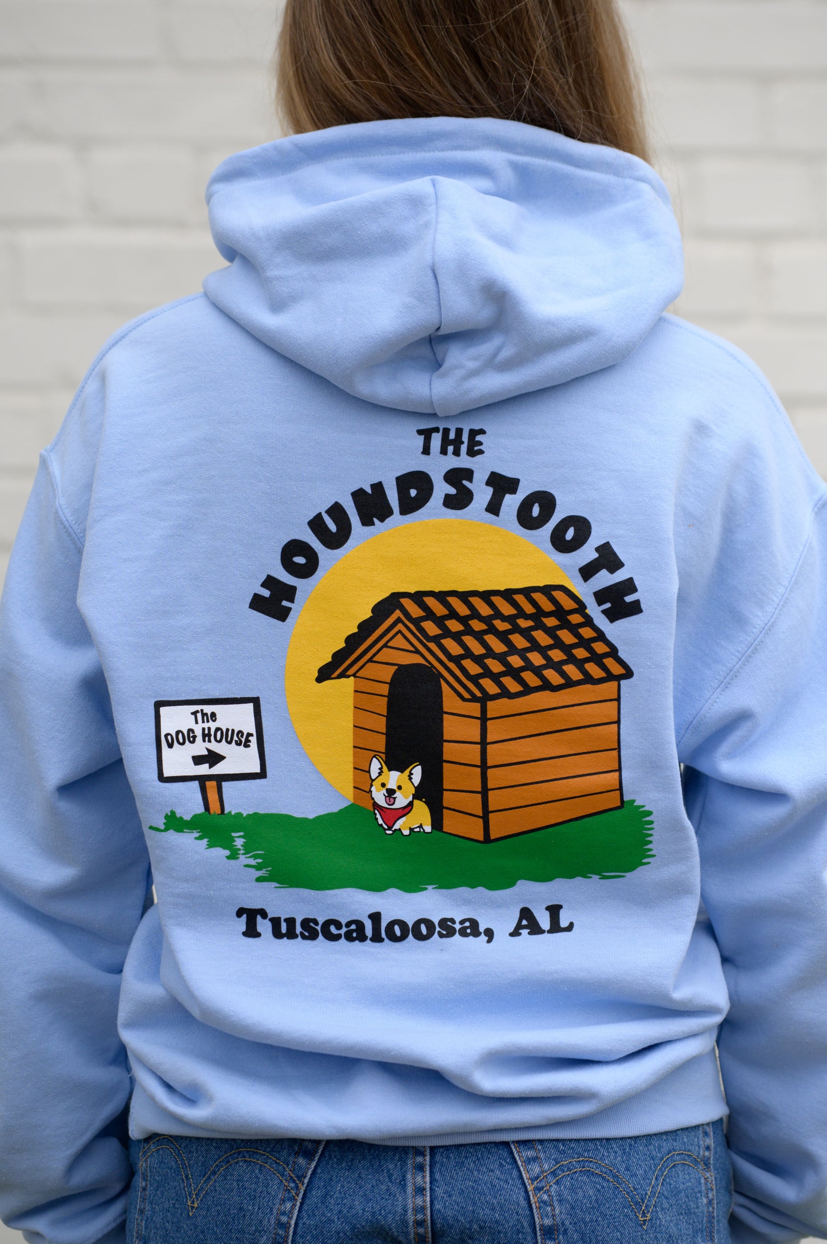 The Houndstooth Light Blue Hoodie with Black text "The Houndstooth" above an image of a corgi standing outside of a dog house