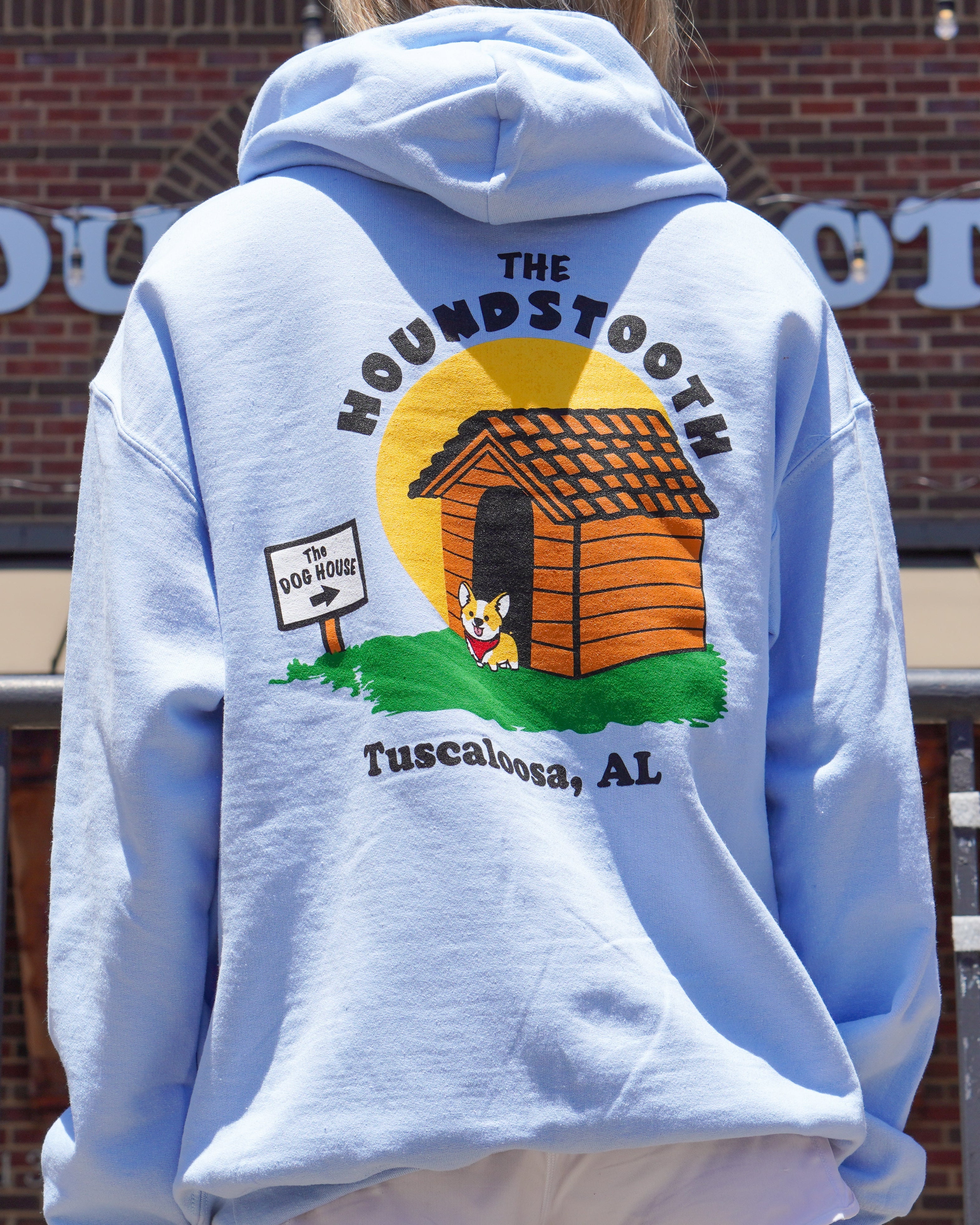 The Houndstooth Light Blue Hoodie with Black text "The Houndstooth" above an image of a corgi standing outside of a dog house