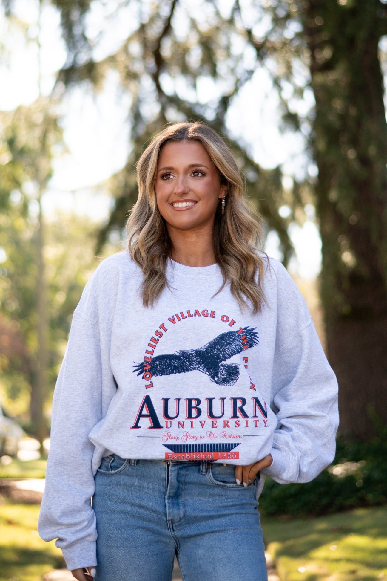 Auburn University Grey Sweatshirt with an image of an eagle flying under Orange text “Loveliest Village of the Plains” and above text “Auburn University”