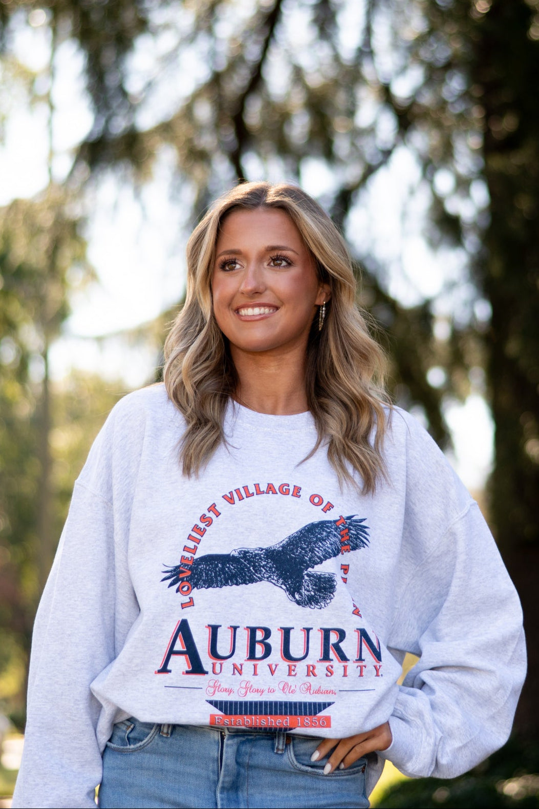 Auburn University Grey Sweatshirt with an image of an eagle flying under Orange text “Loveliest Village of the Plains” and above text “Auburn University”