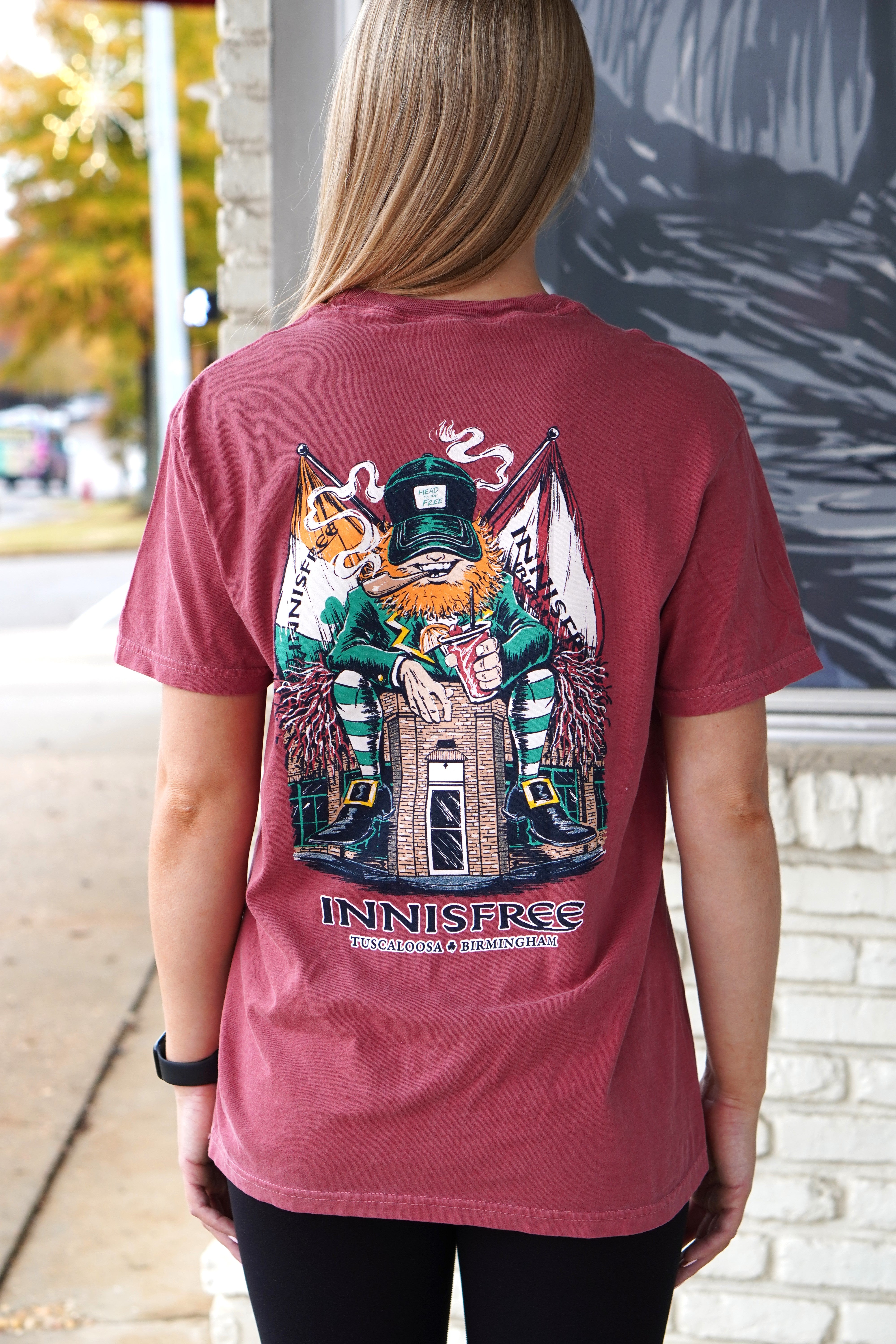 Innisfree Crimson Lucky Leprechaun T-Shirt with an image of a leprechaun sitting on top of the Innisfree Building 