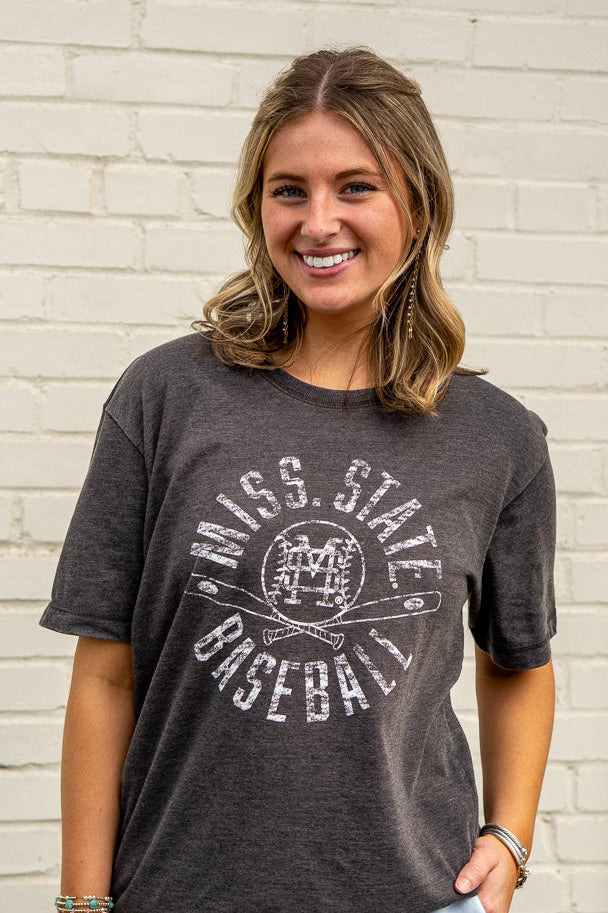 Woman wearing a dark gray t-shirt with 'Mississippi State Baseball' text against a white brick wall.