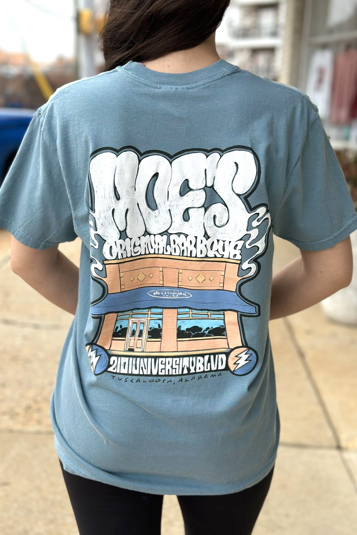 Moe's Ice Blue T-Shirt with White text "Moe's Original Barbeque" above an illustration of the Moe's Building 