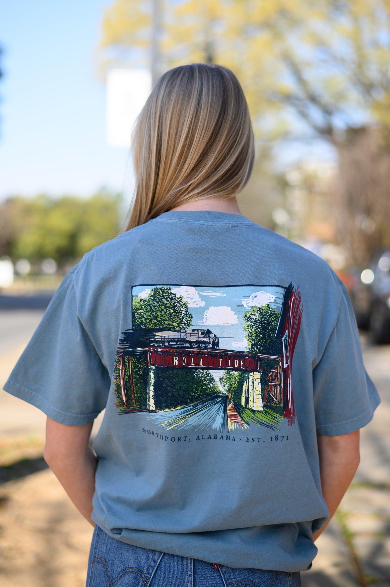 Local Merch Dusty Blue T-Shirt with a hand-drawn illustration of the Downtown Northport Train tracks above Black text "Northport, Alabama EST. 1871"