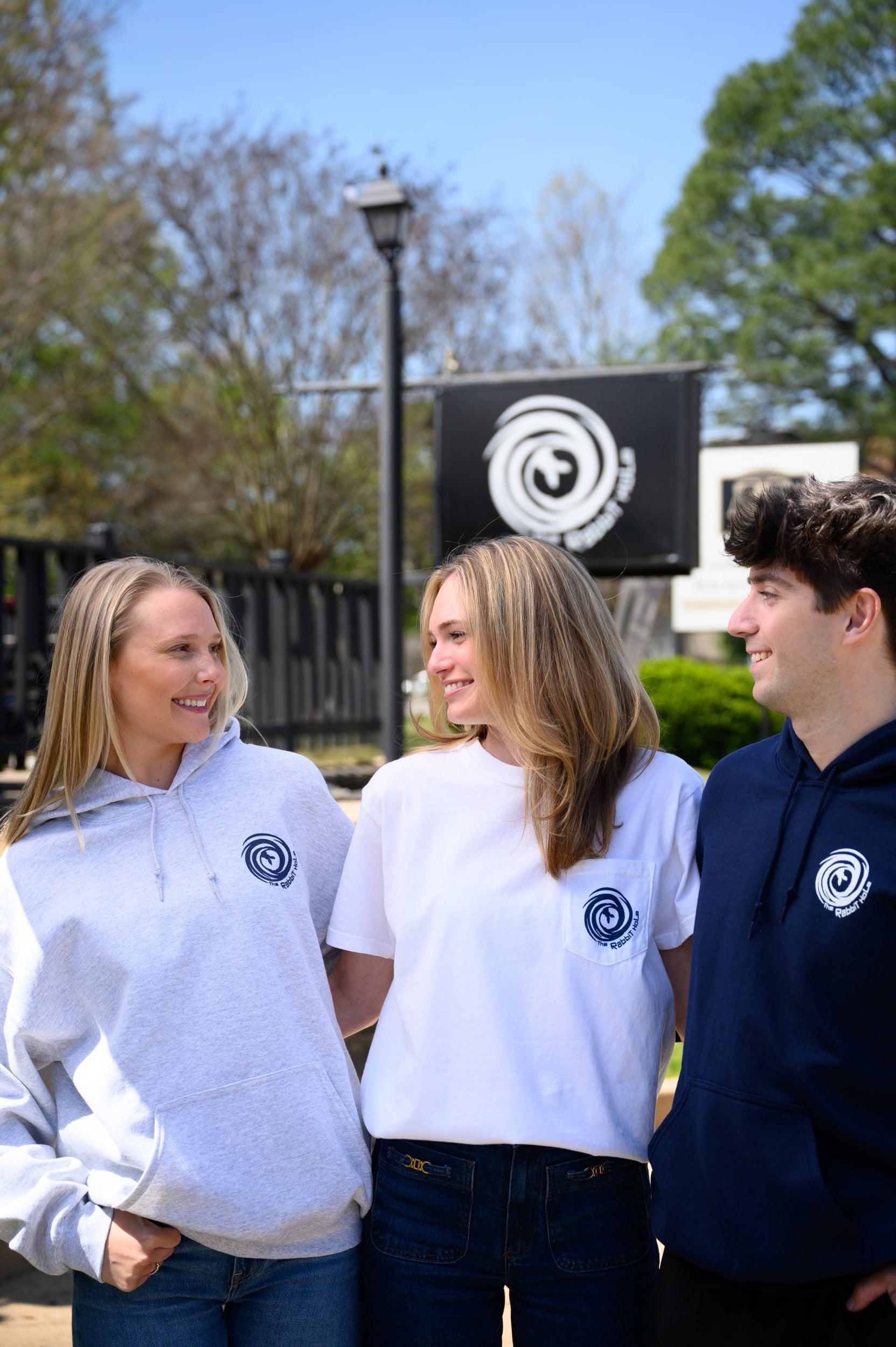 Three people wearing out Rabbit Hole products in front of the Rabbit Hole sign