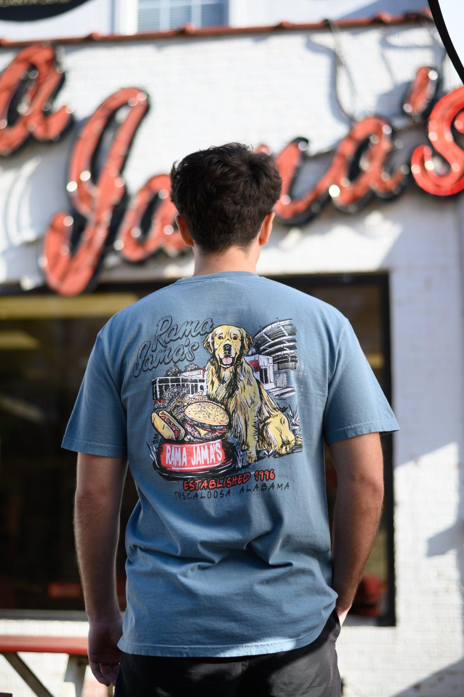 Rama Jama’s Dusty Blue shirt with an illustration of a golden retriever sitting at the picnic tables outside of the building with a cheeseburger and a hotdog