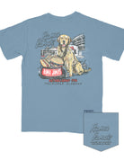 Rama Jama’s Dusty Blue shirt with an illustration of a golden retriever sitting at the picnic tables outside of the building with a cheeseburger and a hotdog