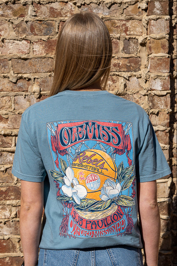 Ole Miss Dusty Light Blue T-Shirt with a basketball card style design featuring a basketball with magnolia flowers in between text “Ole Miss” and “SJB Pavilion”