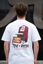 University of Alabama White T-shirt with a Script A brand folding chair that has a red flannel hanging over the back and a play planning board leaning against it. Below, Black text reading “The Tide is Rising”