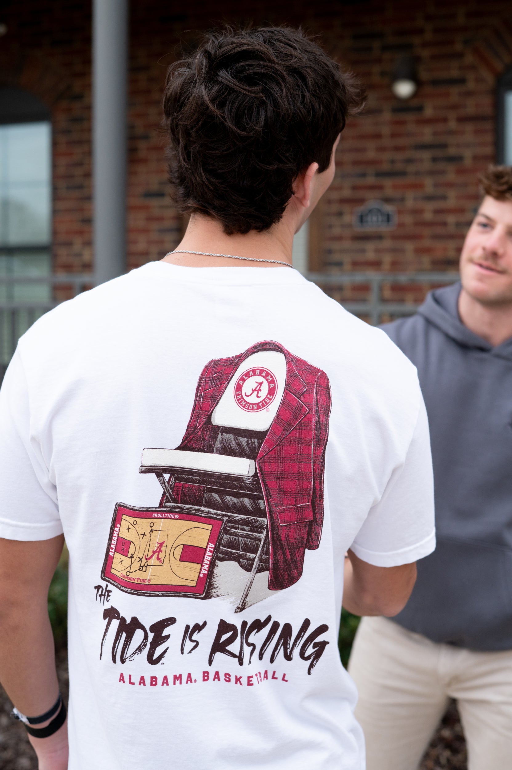 University of Alabama White T-shirt with a Script A brand folding chair that has a red flannel hanging over the back and a play planning board leaning against it. Below, Black text reading “The Tide is Rising”