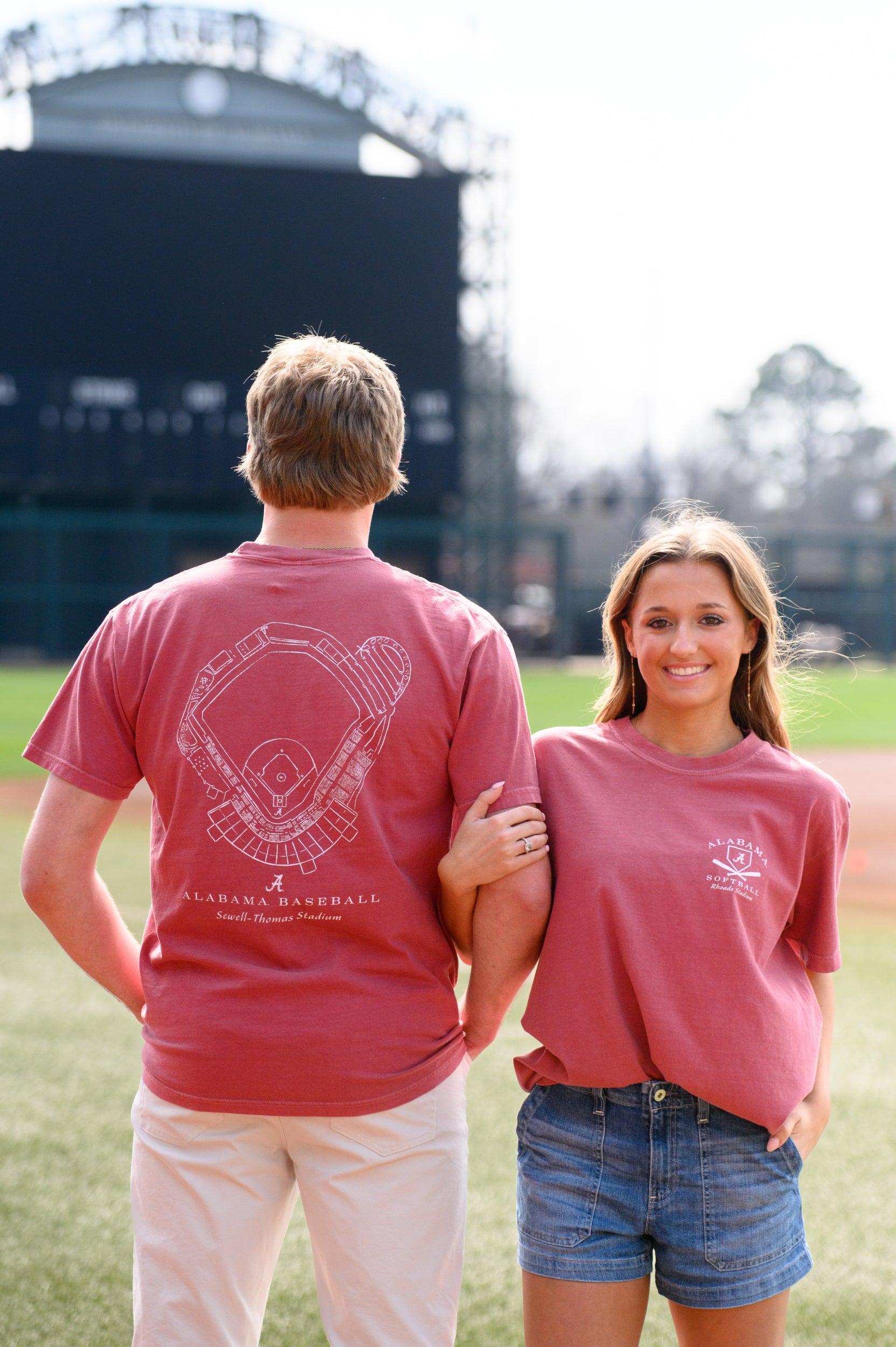 Two people standing on a baseball field wearing matching red t-shirts.