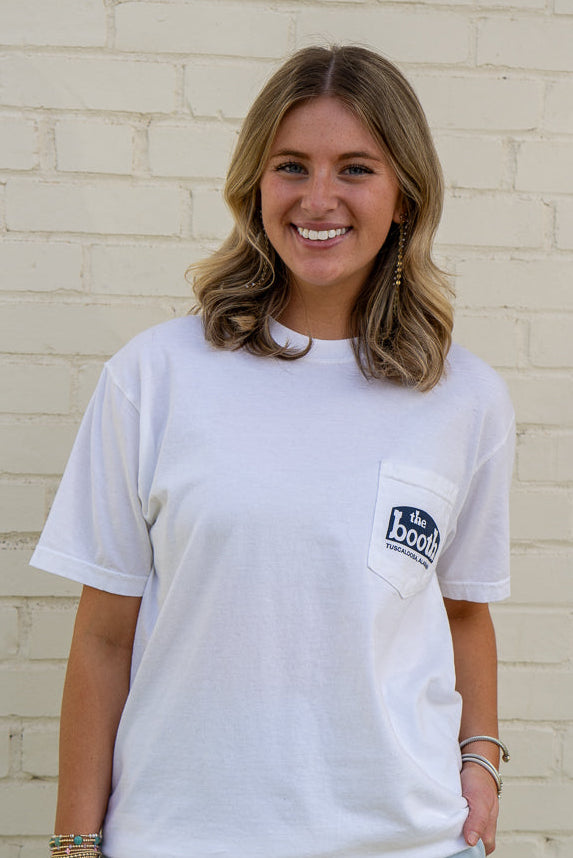 Woman wearing a white t-shirt with a logo, standing against a light brick wall.
