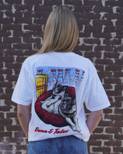 Gallettes White T-Shirt with an illustration of the French Bulldogs Tater and Bean lounging on a dog bed by the bar