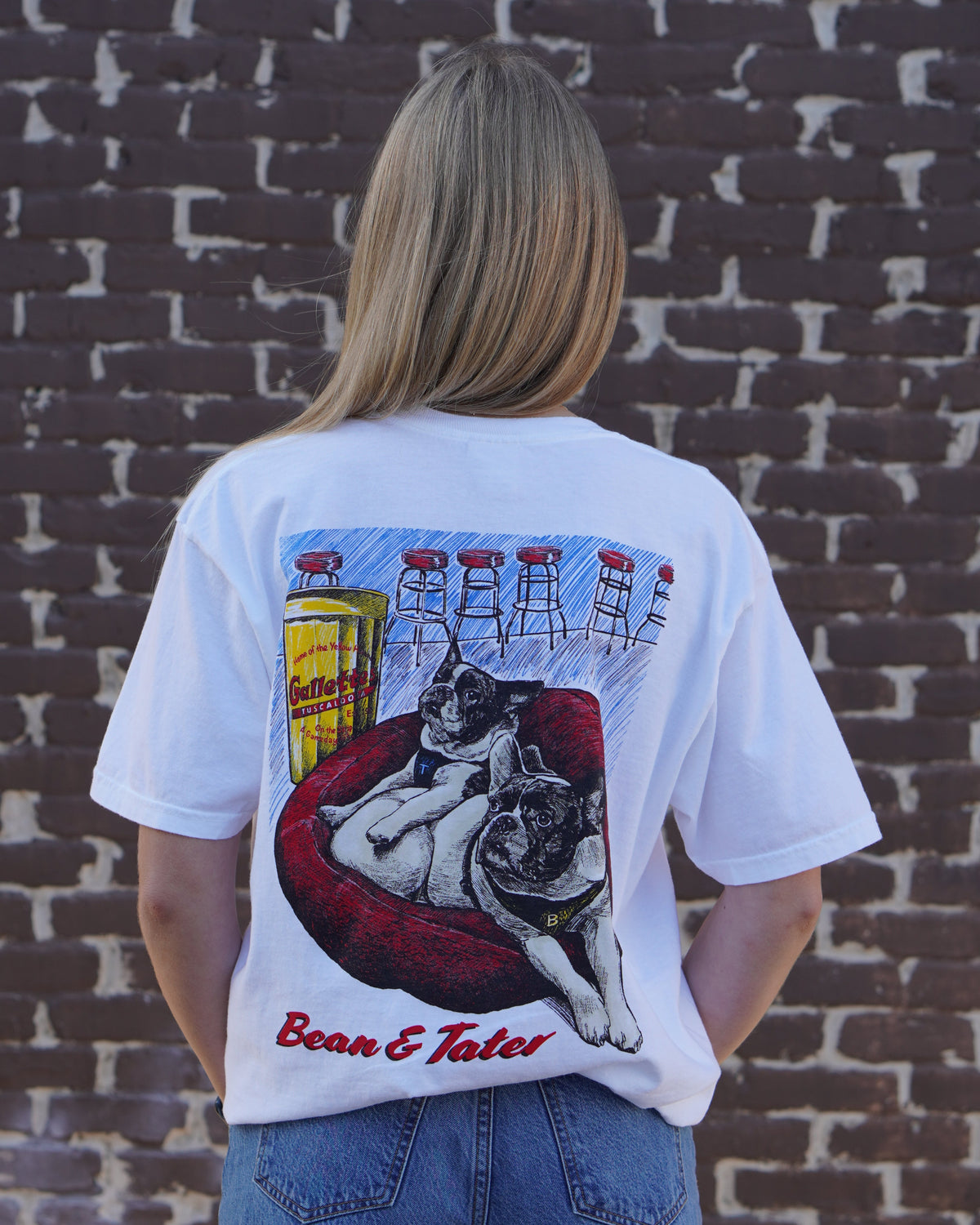 Gallettes White T-Shirt with an illustration of the French Bulldogs Tater and Bean lounging on a dog bed by the bar