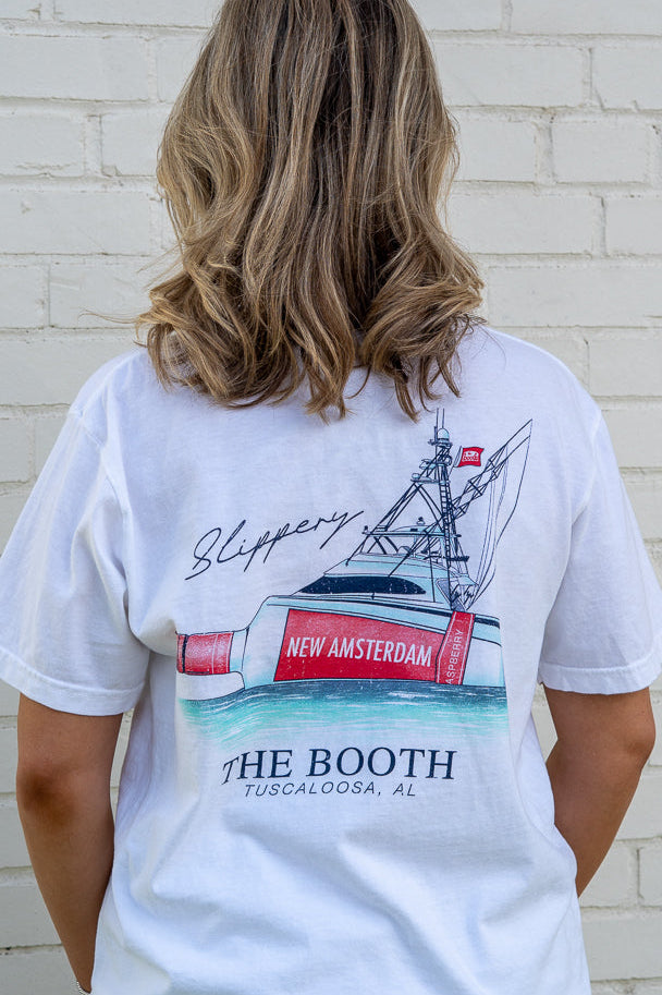 Person wearing a white t-shirt with a graphic design of a ship and text on the back, standing against a white brick wall.