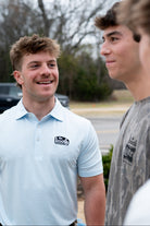 The Booth Light Blue Stripe Men’s Polo with The Booth Logo embroidered on the chest