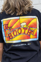 Person wearing a black t-shirt with a colorful graphic design on the back, featuring the word 'BOOTH' and 'Tuscaloosa, AL'.