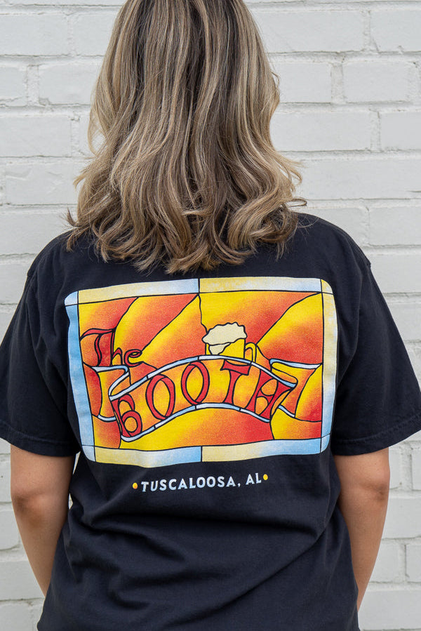 Person wearing a black t-shirt with colorful graphic design on the back, standing against a white brick wall.