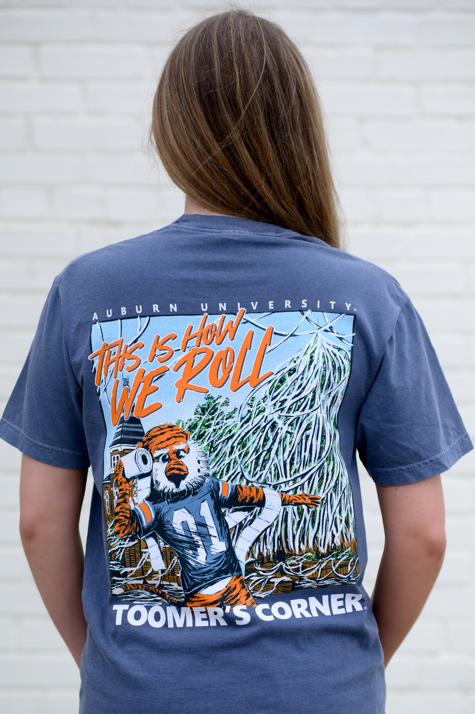 Auburn University Blue This is How We Roll T-Shirt featuring an illustration of Aubie rolling the Toomer's Corner Magnolias beneath Orange text "This Is How We Roll"