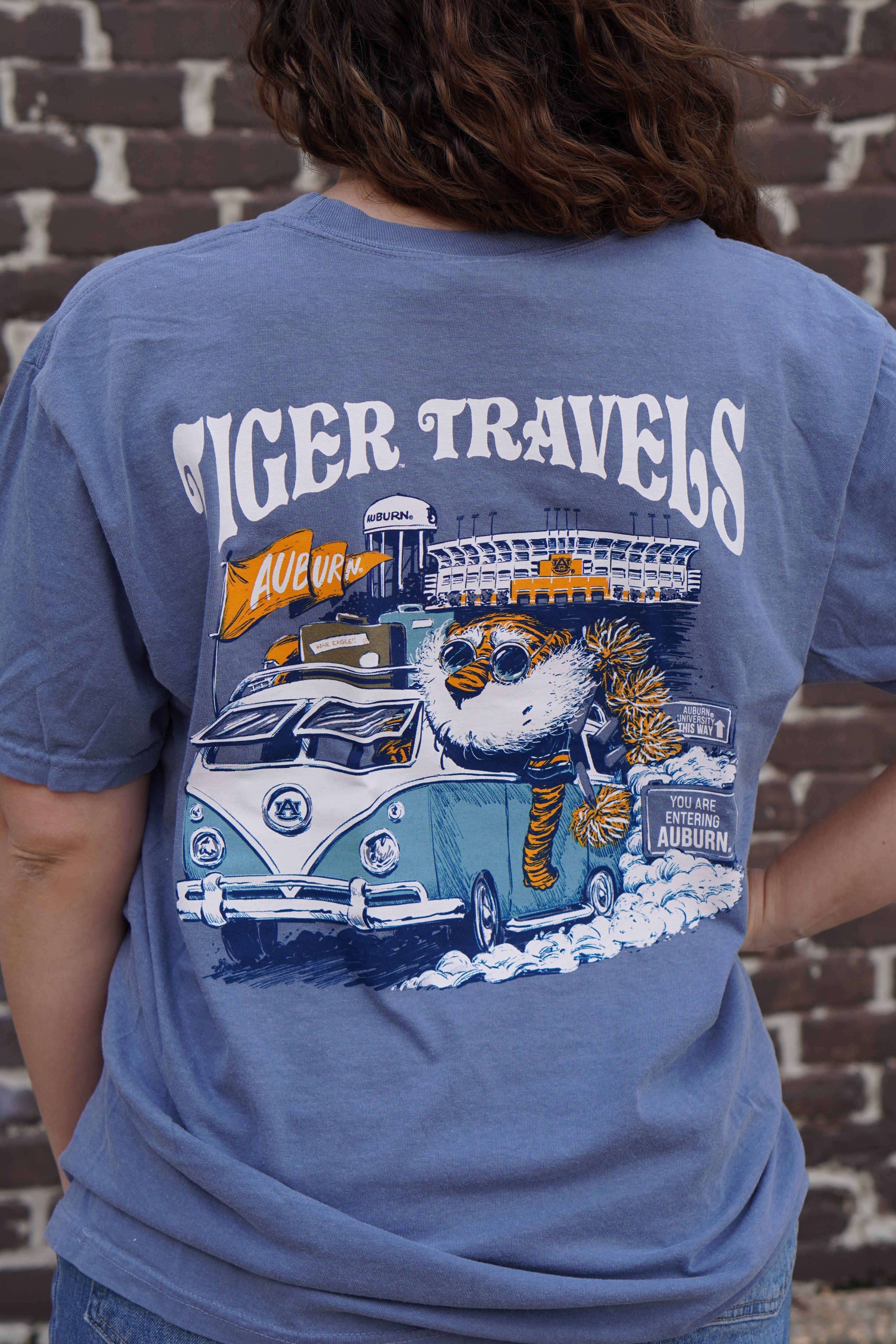 Auburn University Blue T-Shirt with 'Tiger Travels' text and an illustration of  Aubie in a VW Bus leaving the Auburn campus