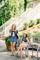 Two women sitting on a wooden deck with a scenic background, wearing our "Tuscaloosa Americana" products